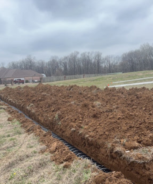 A large field of dirt with a house in the background